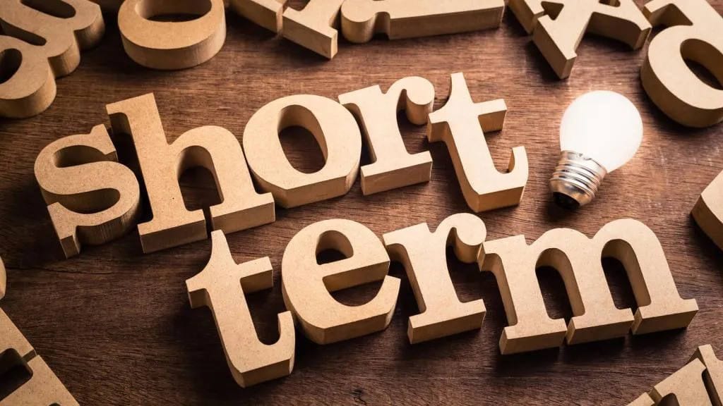 Wooden letters spelling short term next to a glowing light bulb on a wooden table